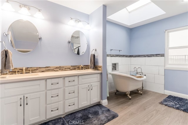 bathroom with hardwood / wood-style flooring, a tub to relax in, vanity, tile walls, and a skylight