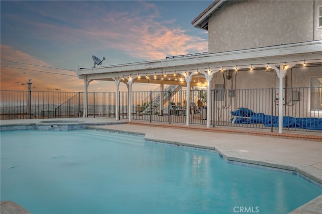 pool at dusk featuring an in ground hot tub and a patio