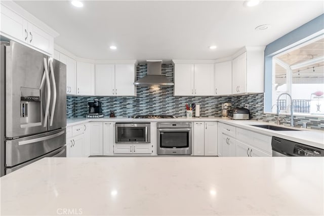 kitchen featuring white cabinetry, stainless steel appliances, wall chimney range hood, and sink