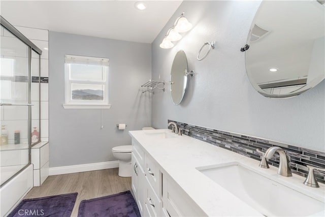 full bathroom with wood-type flooring, combined bath / shower with glass door, toilet, vanity, and decorative backsplash