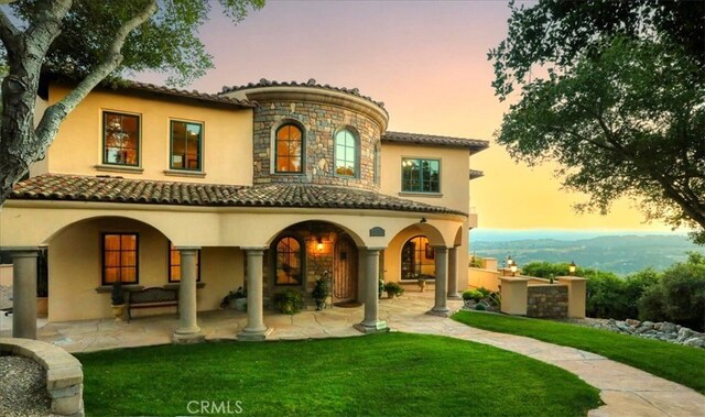 back of property with a lawn, a tiled roof, stucco siding, and stone siding