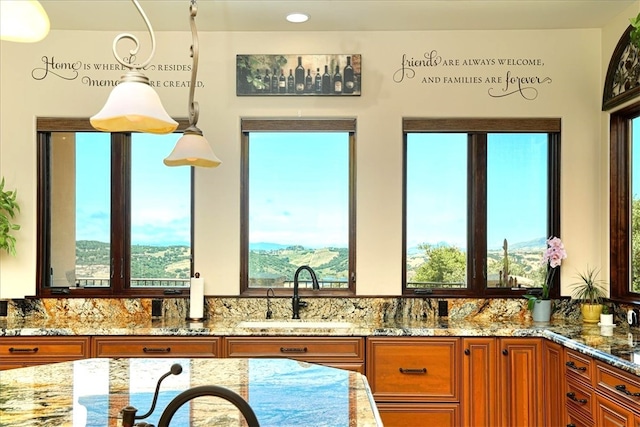 kitchen featuring light stone countertops, pendant lighting, a sink, and brown cabinetry