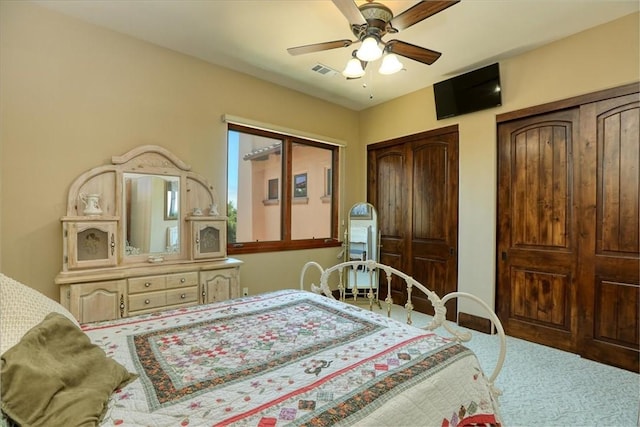 carpeted bedroom featuring a ceiling fan, multiple closets, and visible vents