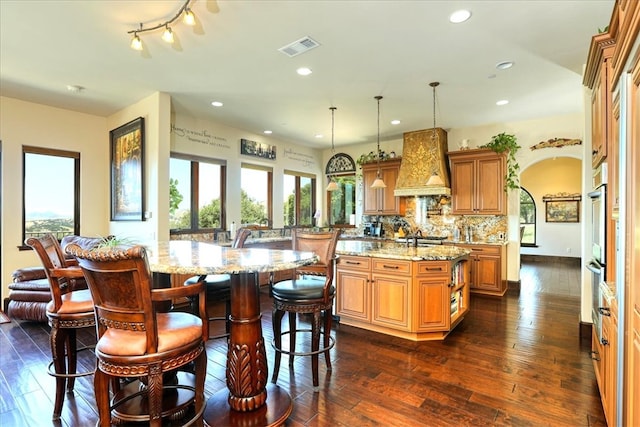 kitchen with a kitchen bar, a center island with sink, visible vents, light stone countertops, and custom exhaust hood