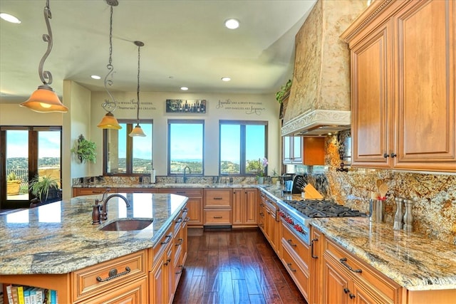 kitchen with stainless steel gas stovetop, dark wood finished floors, a sink, light stone counters, and backsplash