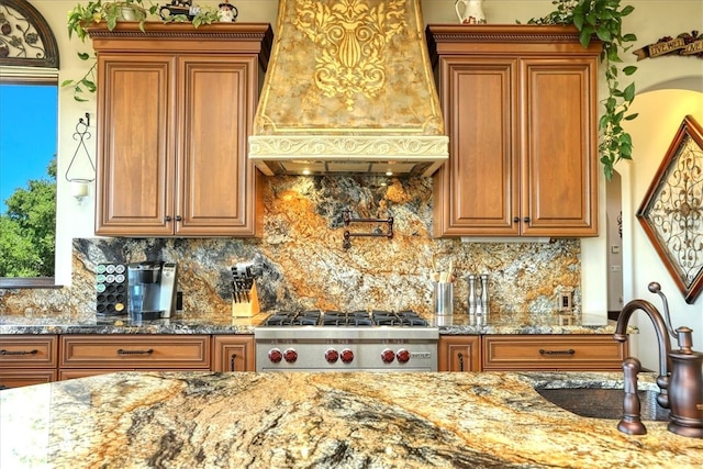 kitchen featuring a sink, stone countertops, custom range hood, and brown cabinets