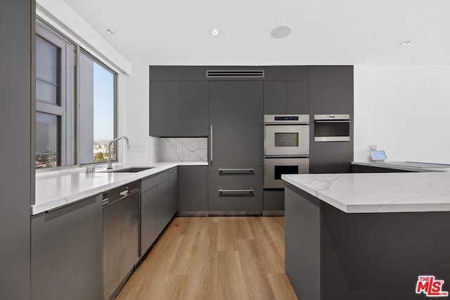 kitchen featuring decorative backsplash, sink, stainless steel dishwasher, light hardwood / wood-style floors, and white double oven