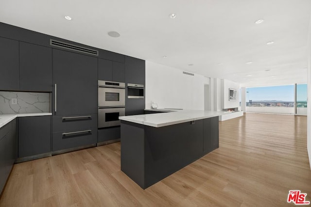 kitchen featuring light stone countertops, light hardwood / wood-style floors, decorative backsplash, and double oven