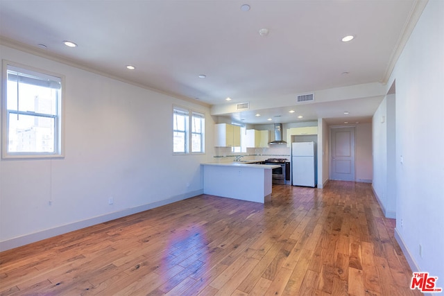 kitchen with wall chimney exhaust hood, white refrigerator, light hardwood / wood-style floors, kitchen peninsula, and white cabinets