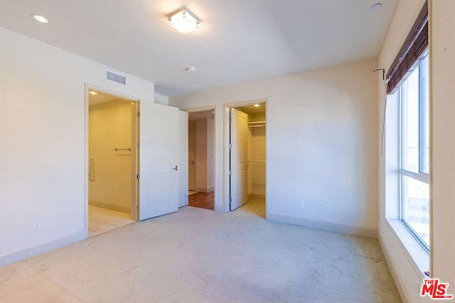 unfurnished bedroom with light colored carpet, a closet, multiple windows, and a spacious closet