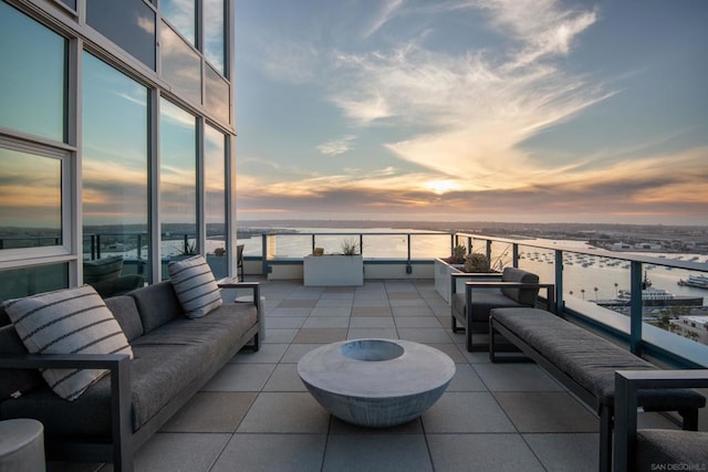 patio terrace at dusk with a balcony, a water view, and an outdoor hangout area