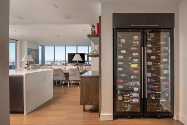 wine cellar with a wall of windows, light hardwood / wood-style flooring, and beverage cooler