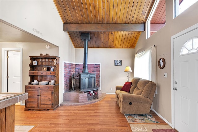 living room featuring beamed ceiling, light hardwood / wood-style flooring, a wood stove, and wooden ceiling