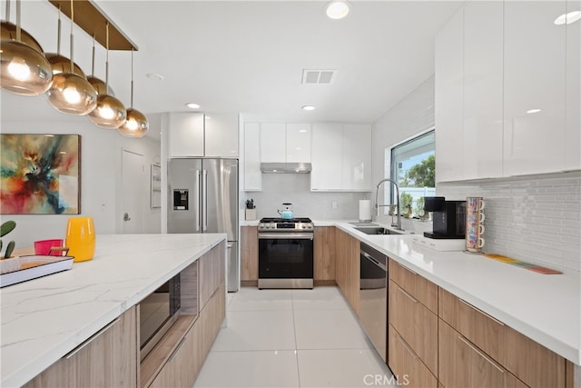 kitchen featuring white cabinets, light tile patterned flooring, sink, decorative light fixtures, and stainless steel appliances