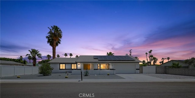 view of front of property featuring a garage, concrete driveway, fence private yard, and roof mounted solar panels