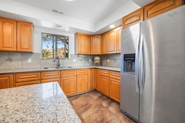 kitchen with tasteful backsplash, light stone countertops, sink, and stainless steel refrigerator with ice dispenser