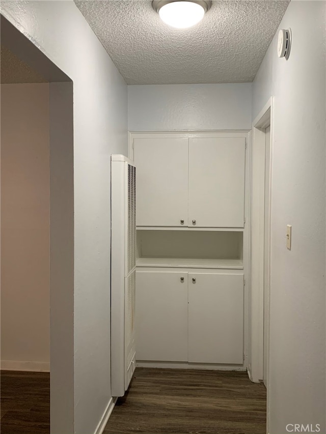 hall with a textured ceiling and dark hardwood / wood-style flooring