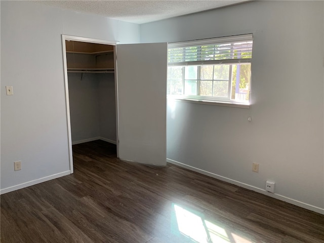 unfurnished bedroom featuring a closet, a textured ceiling, a walk in closet, and dark hardwood / wood-style floors