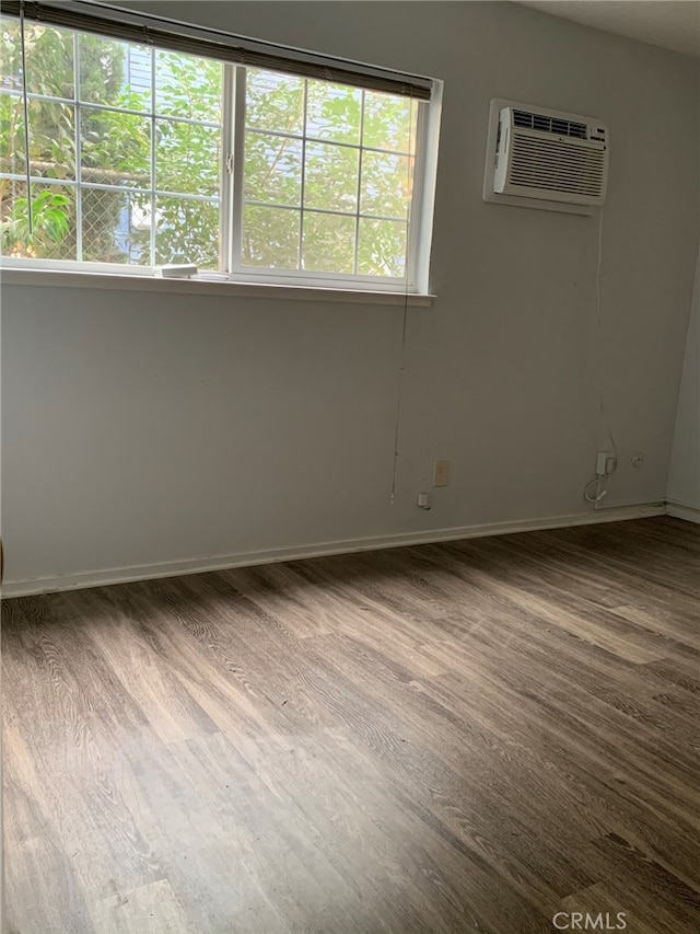 spare room with an AC wall unit, wood-type flooring, and a healthy amount of sunlight