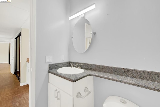 bathroom featuring parquet floors, vanity, and toilet