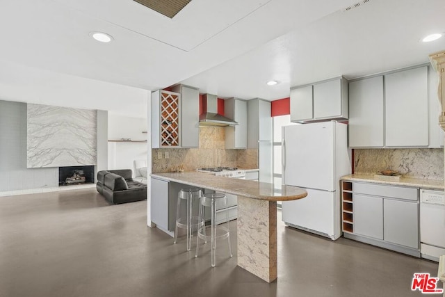 kitchen with wall chimney range hood, appliances with stainless steel finishes, decorative backsplash, and a kitchen breakfast bar