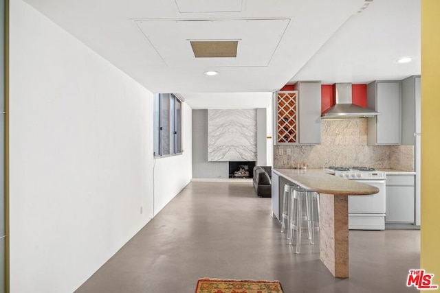 kitchen featuring decorative backsplash, wall chimney exhaust hood, white range oven, and a breakfast bar area