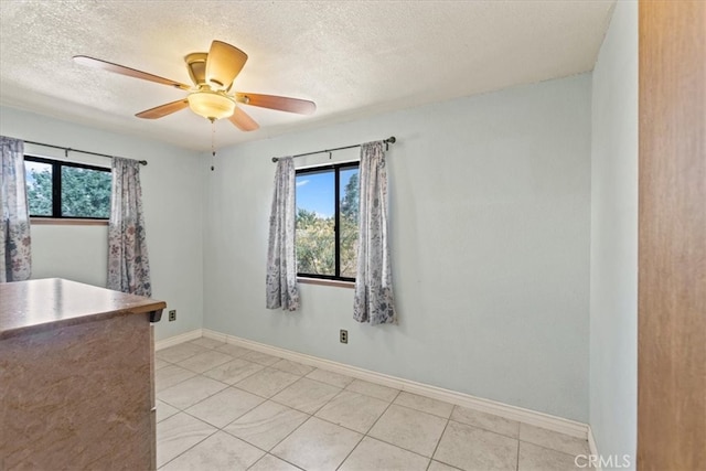 empty room with ceiling fan, a textured ceiling, and light tile patterned floors