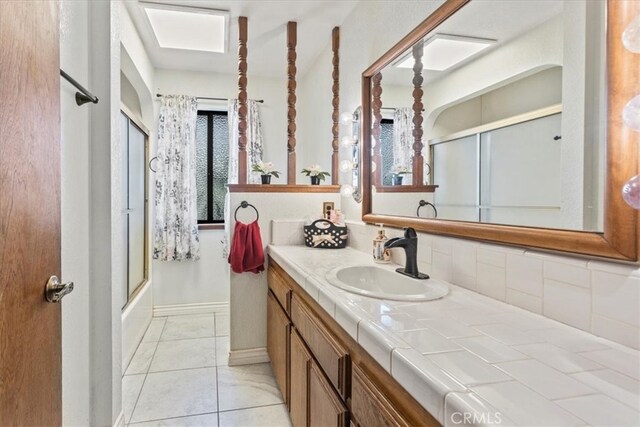 bathroom with vanity, decorative backsplash, tile patterned floors, and shower / bath combination with glass door