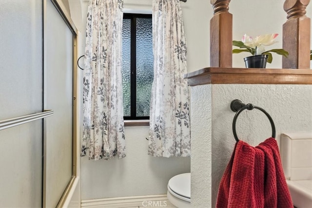 bathroom with toilet and shower / bath combination with glass door