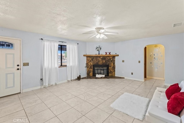 tiled living room featuring ceiling fan, a stone fireplace, and a textured ceiling