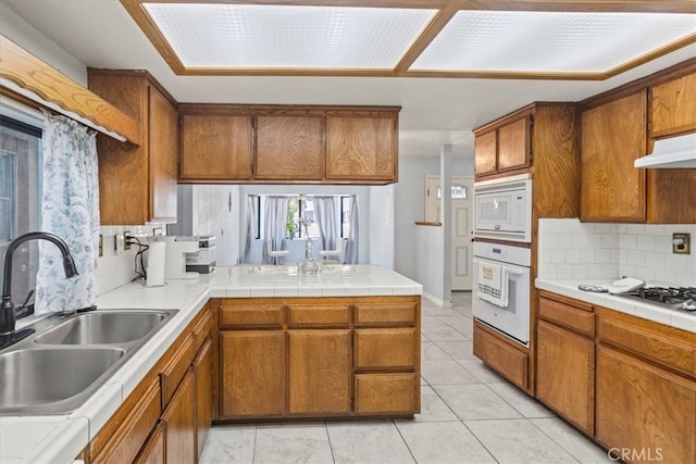 kitchen with kitchen peninsula, decorative backsplash, light tile patterned floors, sink, and white appliances