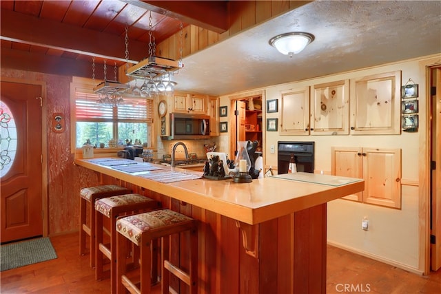 kitchen with beamed ceiling, black oven, hardwood / wood-style floors, sink, and a kitchen bar