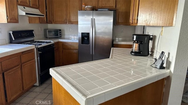 kitchen with stainless steel fridge, black range with gas stovetop, and tile counters