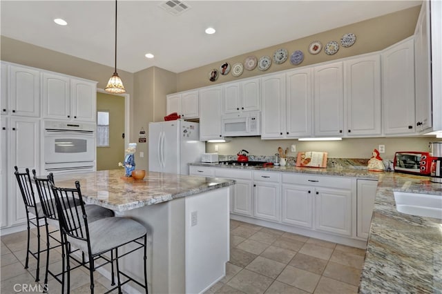 kitchen featuring white cabinets, light stone countertops, decorative light fixtures, and white appliances