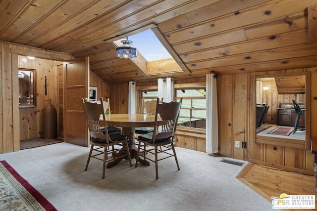 dining space featuring light carpet, wood walls, and a skylight