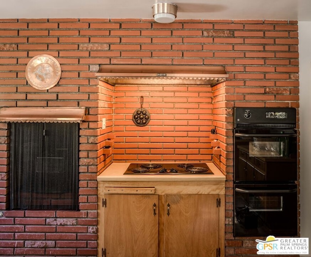 kitchen featuring electric cooktop, double oven, and brick wall