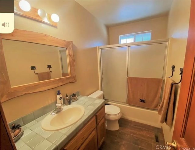 full bathroom featuring hardwood / wood-style flooring, vanity, toilet, and bath / shower combo with glass door