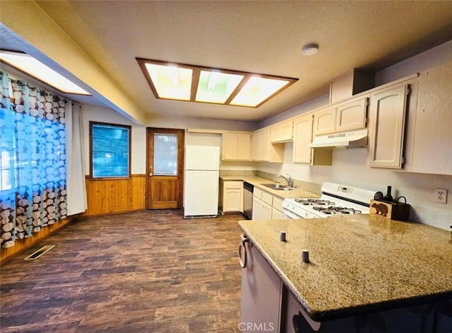 kitchen with light stone countertops, sink, dark wood-type flooring, wood walls, and white appliances