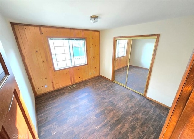 unfurnished bedroom featuring dark hardwood / wood-style flooring, wooden walls, and a closet