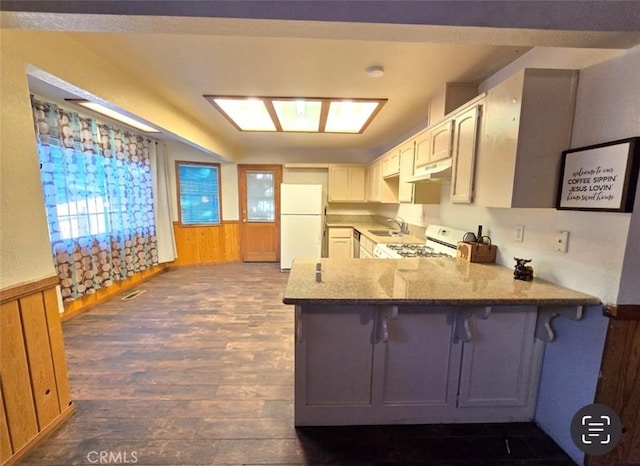 kitchen with light stone countertops, dark hardwood / wood-style floors, kitchen peninsula, wood walls, and white appliances