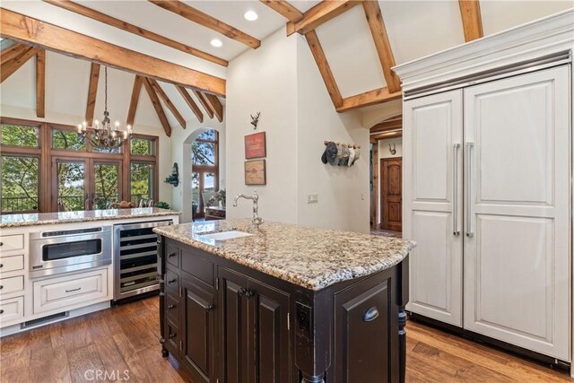 kitchen featuring dark hardwood / wood-style floors, beam ceiling, an island with sink, sink, and beverage cooler