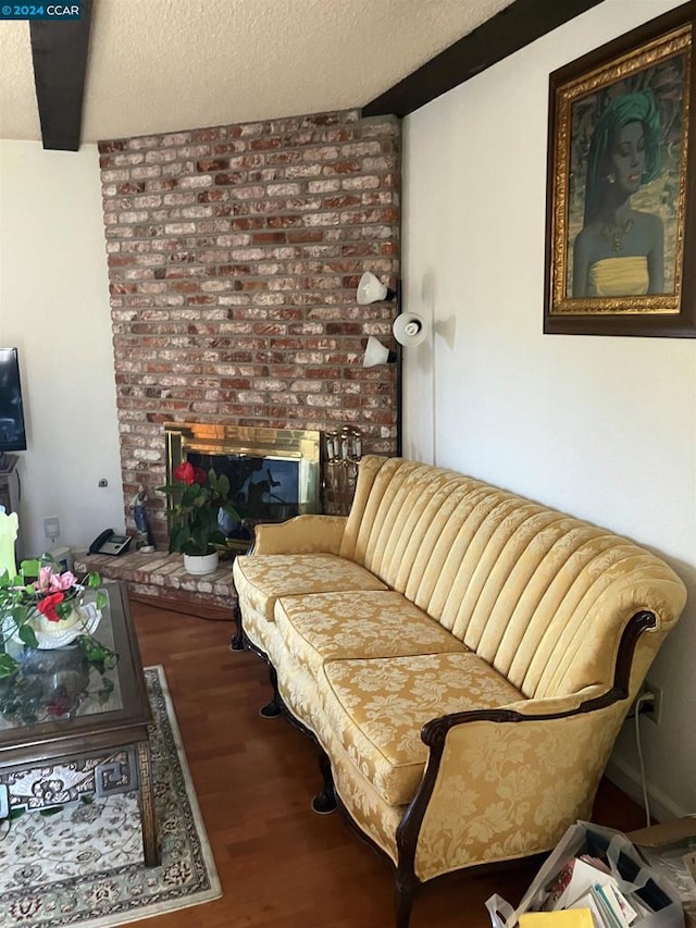 living room with hardwood / wood-style flooring, a textured ceiling, beamed ceiling, and a brick fireplace