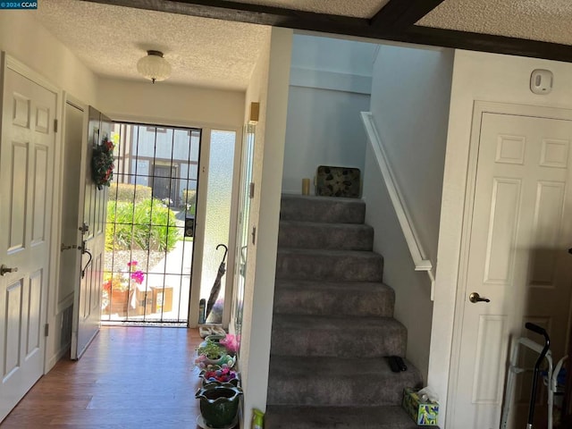 stairs featuring beam ceiling, hardwood / wood-style flooring, and a textured ceiling