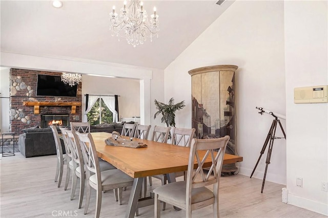 dining room with light wood-type flooring, high vaulted ceiling, a brick fireplace, and an inviting chandelier