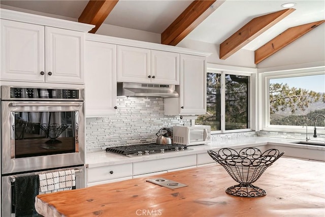 kitchen featuring white cabinetry, sink, vaulted ceiling with beams, decorative backsplash, and appliances with stainless steel finishes