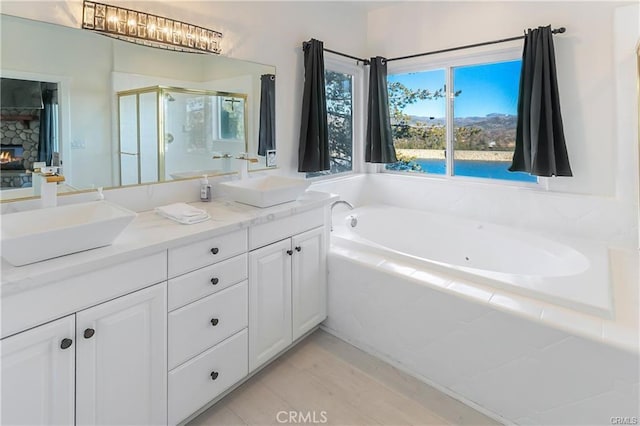 bathroom featuring vanity, a stone fireplace, and shower with separate bathtub