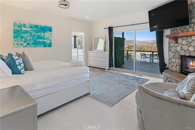 bedroom featuring light hardwood / wood-style floors, access to exterior, a fireplace, and ensuite bath