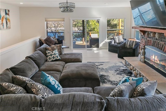 living room featuring a stone fireplace, a notable chandelier, and hardwood / wood-style flooring