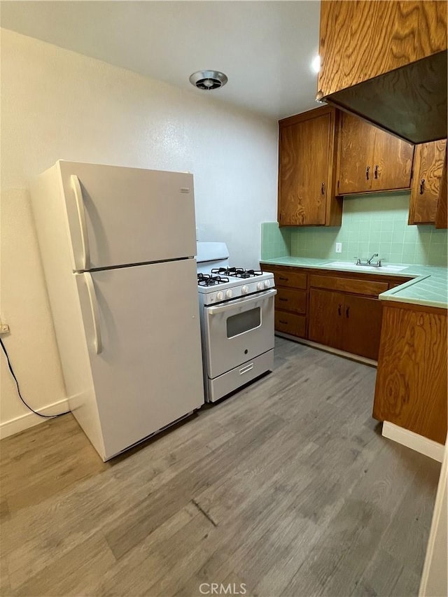 kitchen featuring light wood-type flooring, white appliances, backsplash, and sink