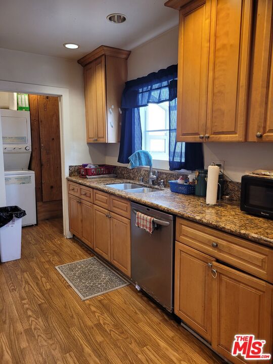 kitchen featuring sink, dishwasher, dark stone countertops, light wood-type flooring, and stacked washer and dryer